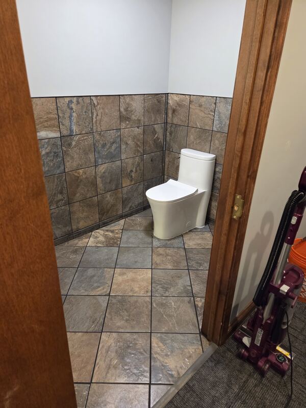 Small bathroom with a white toilet, stone-look tile floor set on the diagonal and tile on the lower walls.