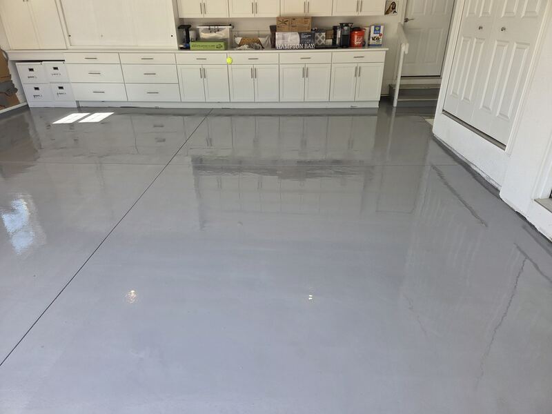 Finished glossy light gray epoxy garage floor with white cabinets along the back wall.