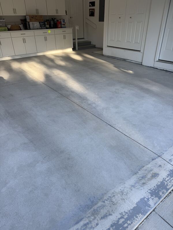 Garage with a bare gray concrete floor, white cabinets along the back wall and two steps up to a door.