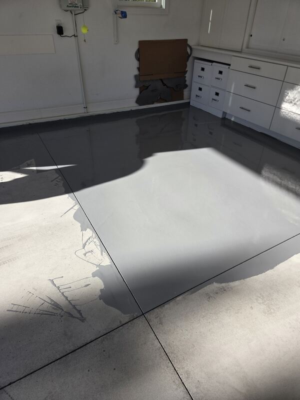 Garage floor partly coated. Glossy gray epoxy on one side, bare concrete in the foreground.